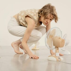 Young woman observing several table fans in minimalist indoor studio setting.