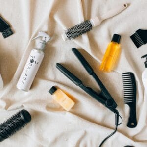Flat lay image of various hair care products and tools on a textured fabric surface.